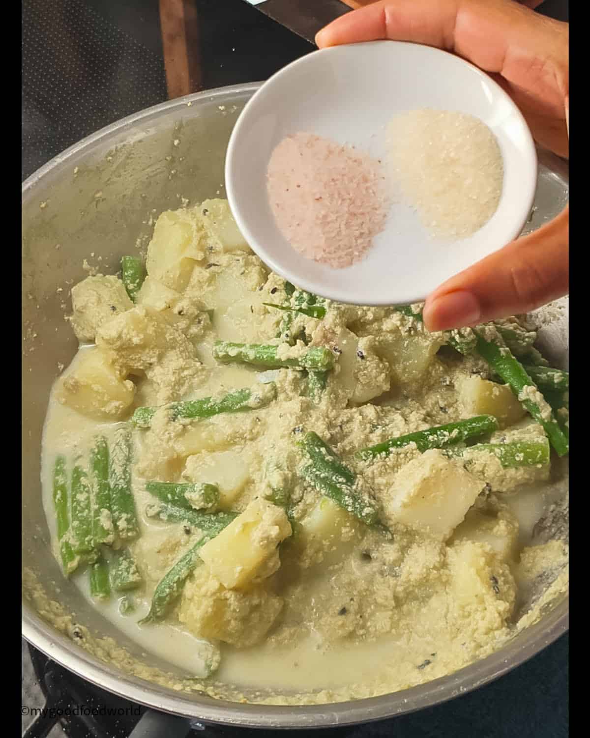 Adding sugar and salt to the potatoes and green beans that are cooking in the pan below.