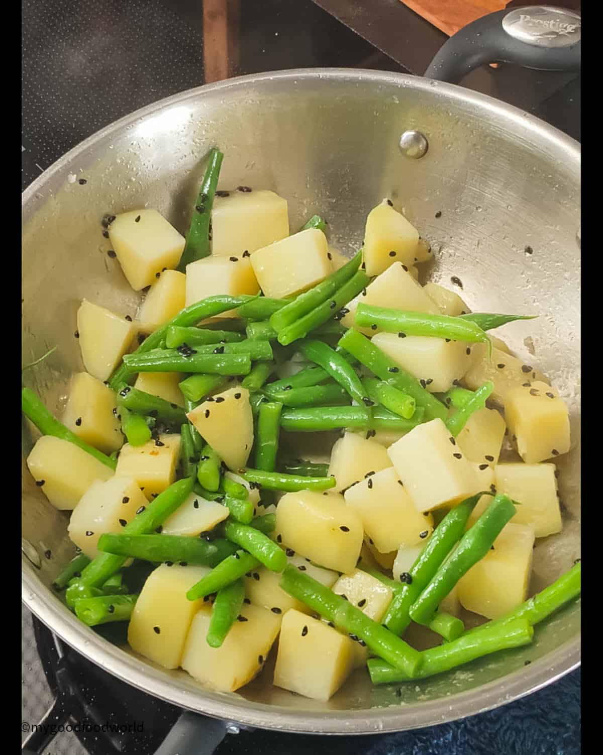 Some green beans and potatoes are frying in oil with some nigella seeds.