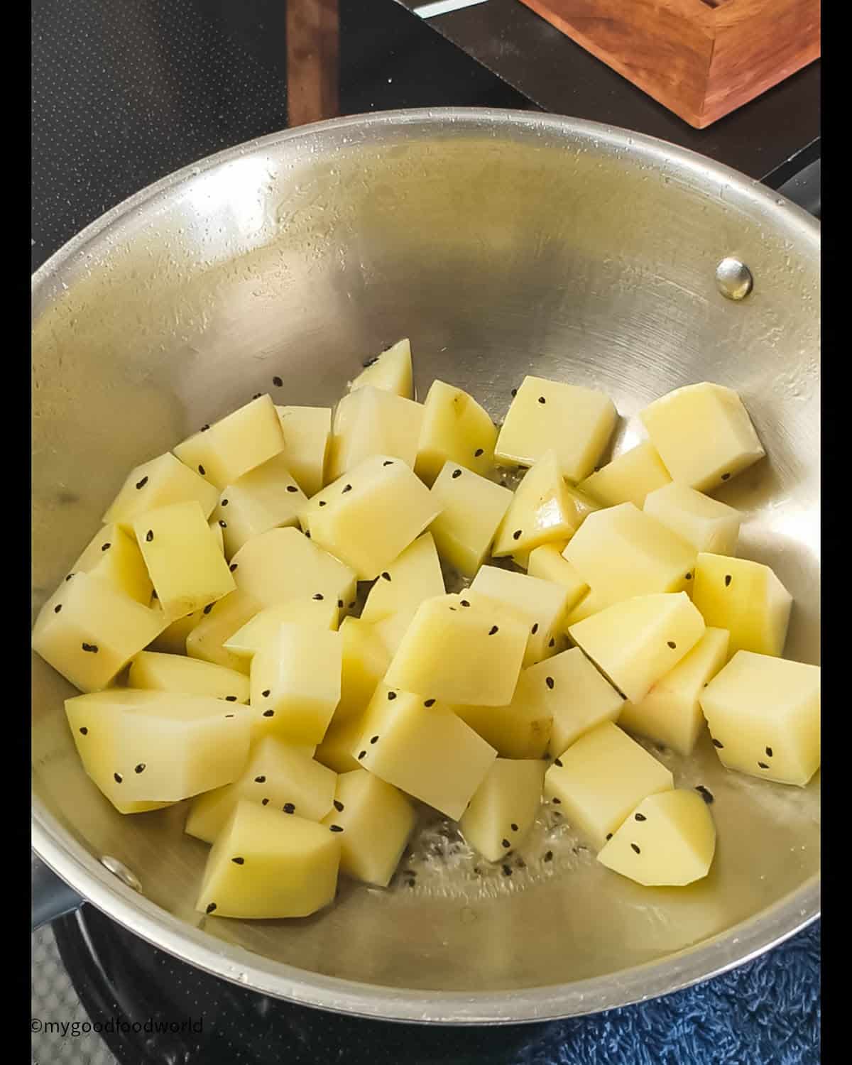 Cubes of potatoes are being sauteed in some oil and kala jeera.