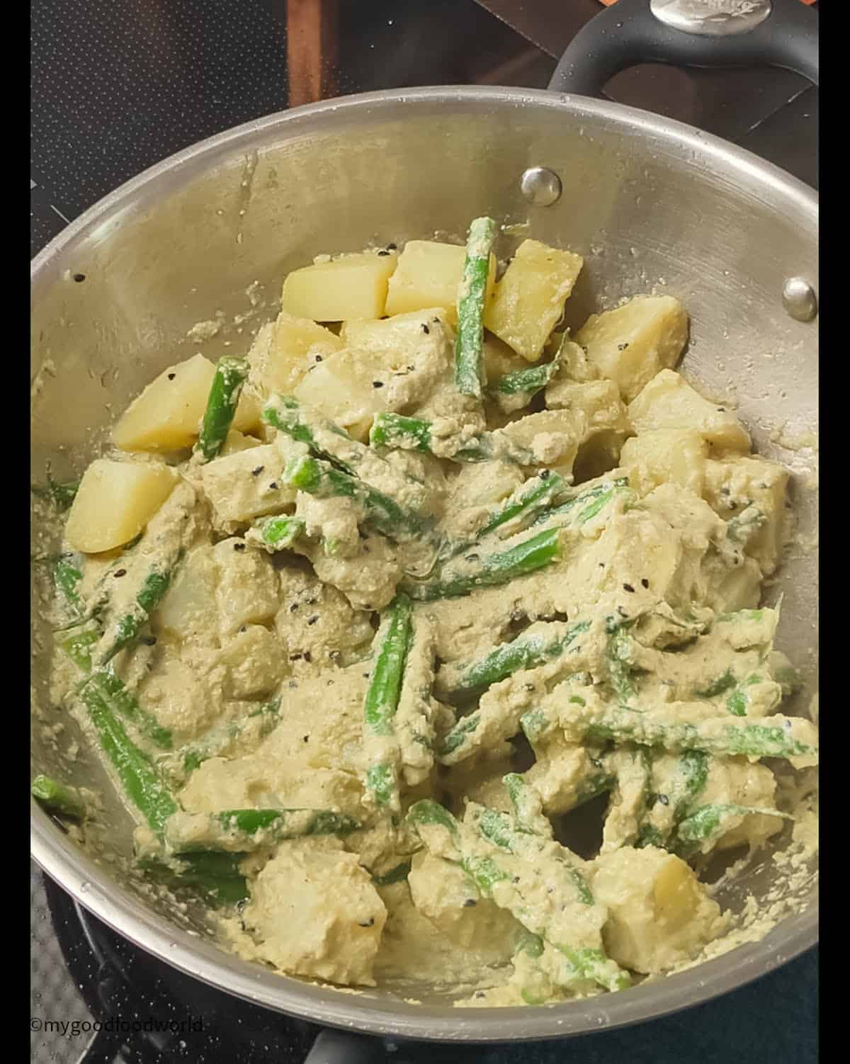 Creamy poppy seed pasta is cooking with cubed potatoes and green beans in a pan.