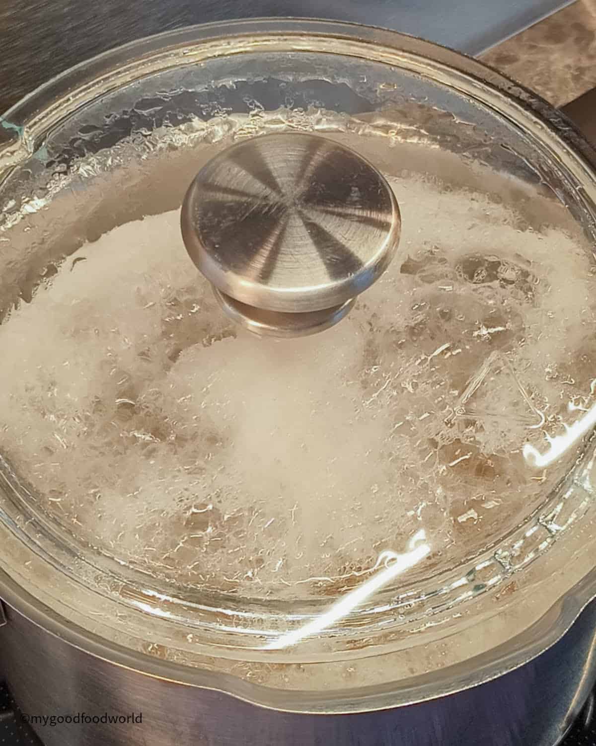 Chickpeas are cooking in a large pot with its lid ajar and foam forming on top.