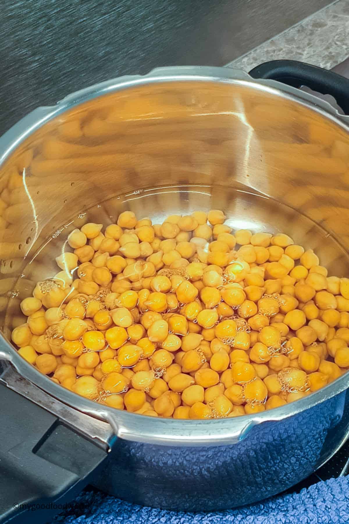 Soaked garbanzo beans are placed in a pressure cooker with water for cooking.