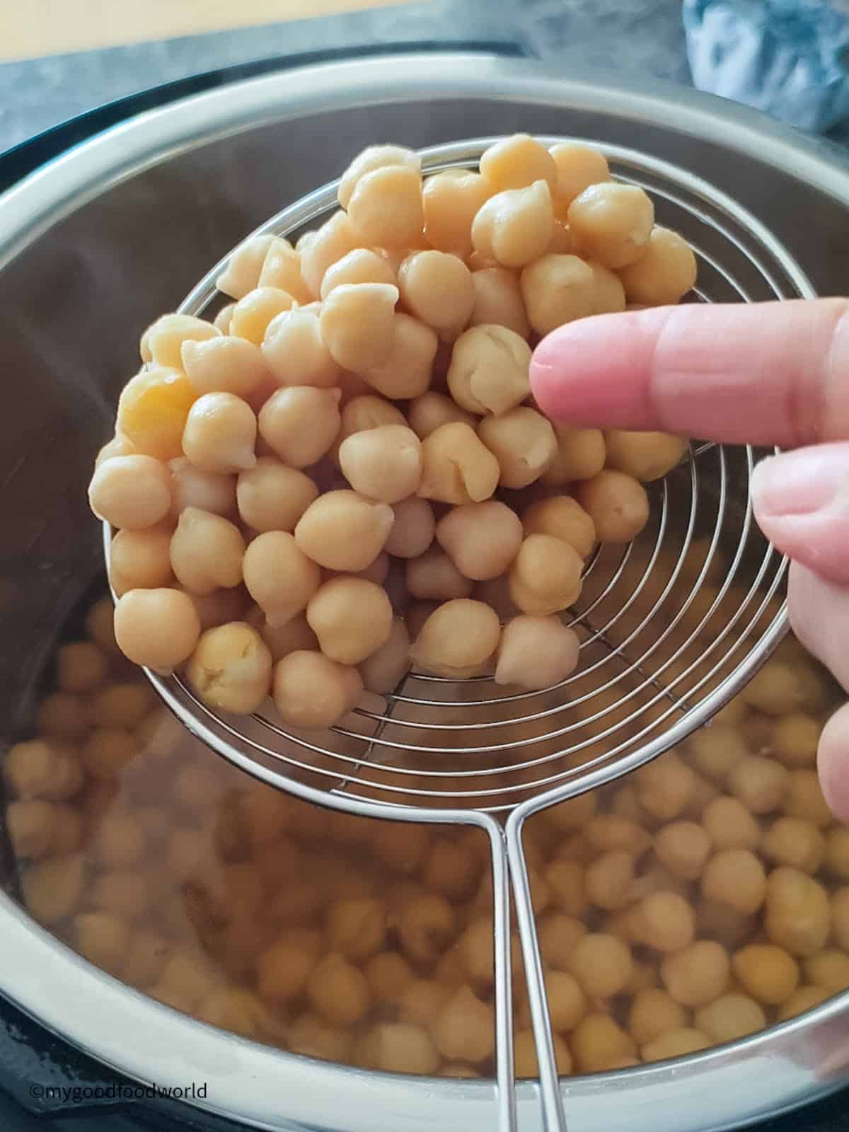 Perfectly cooked, tender chickpeas are being scooped with a slotted ladle.
