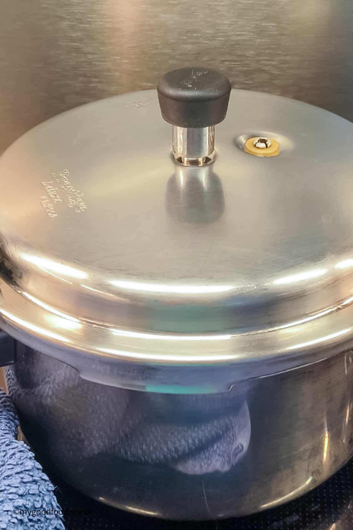 A stovetop pressure cooker has its lid on and valve placed on top for pressure cooking.