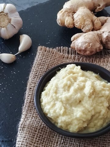 To learn how to make ginger garlic paste at home, some fresh ginger, garlic, and puree are placed on a table.
