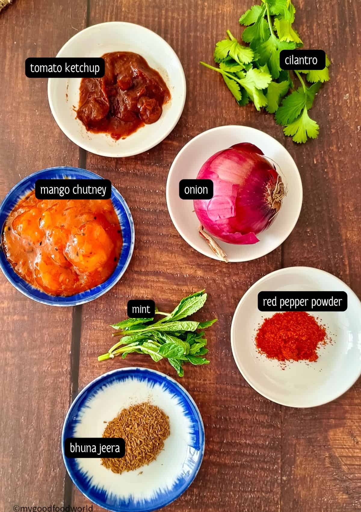 Onion salad for poppadoms, ingredients such as red onion, mango chutney, and tomato ketchup are placed on a wooden table.