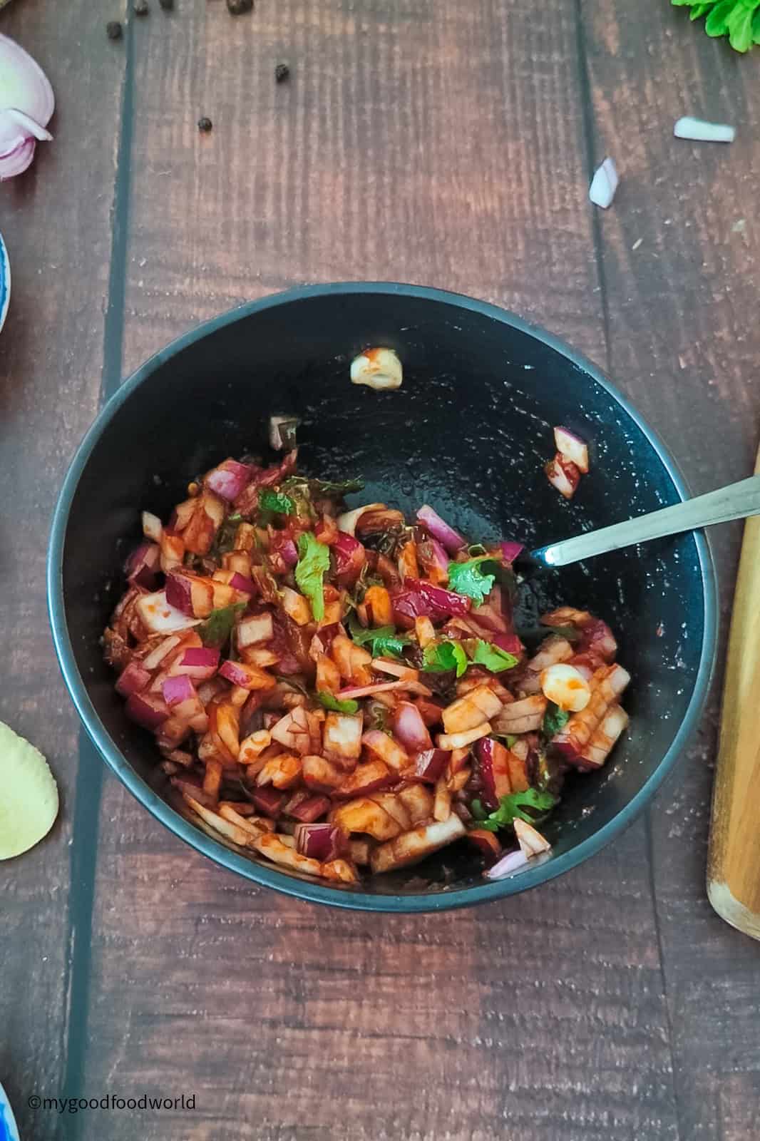 Takeaway-style Indian onion salad is being mixed with a spoon in a bowl.