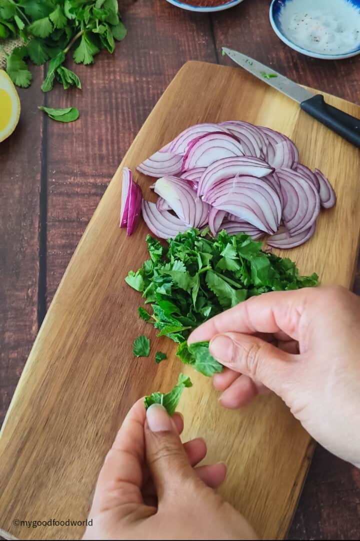 Finely sliced onions, cilantro, and mint leaves are placed on a wooden board.