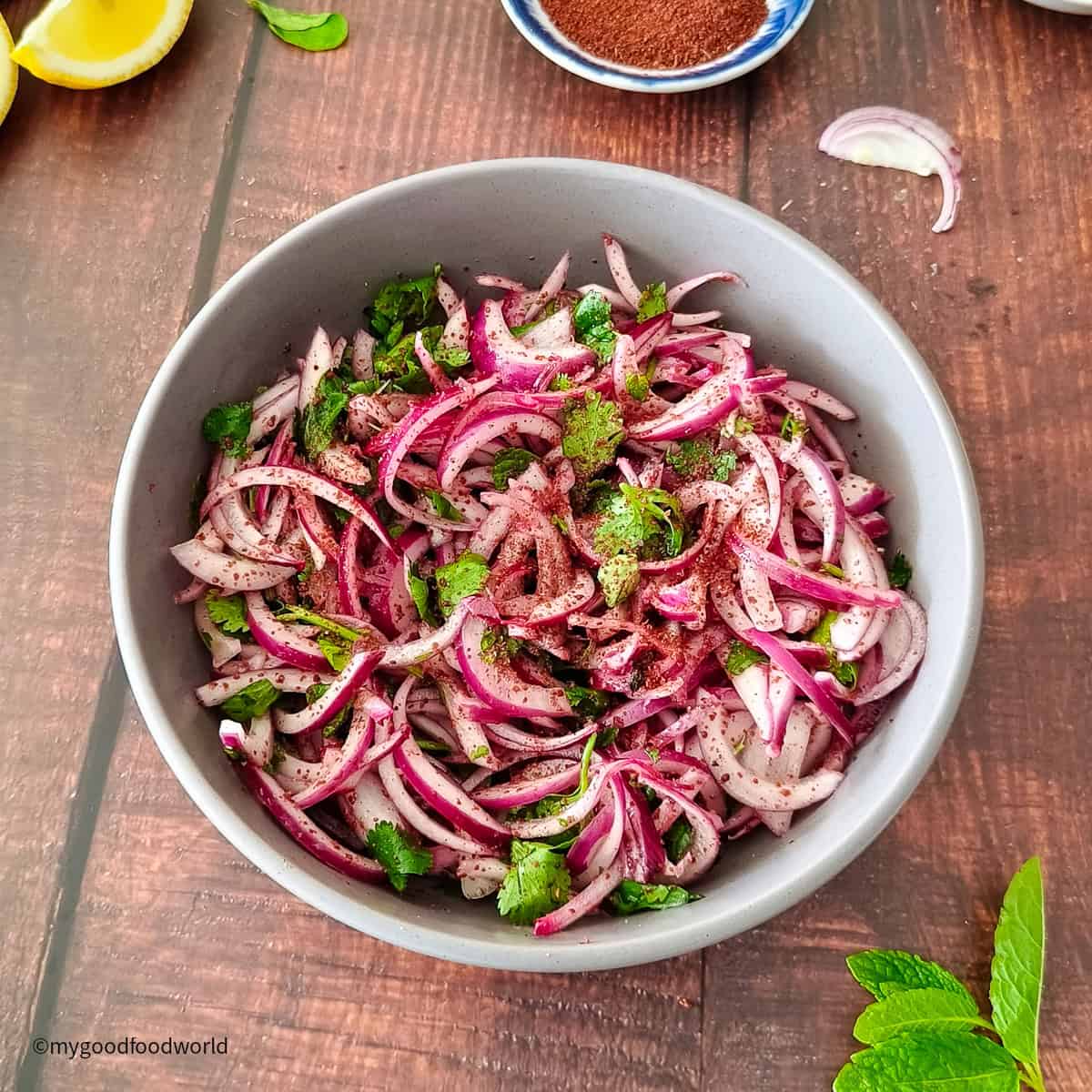 A close-up image of Mediterranean-style sumac onion salad with mint leaves and fresh lemon.