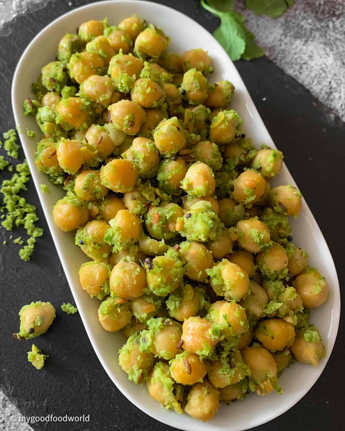 South Indian chickpea sundal served in a white oval bowl garnished with fresh coconut and curry leaves.