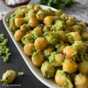 Chickpea sundal in a black bowl garnished with fresh coconut and curry leaves.