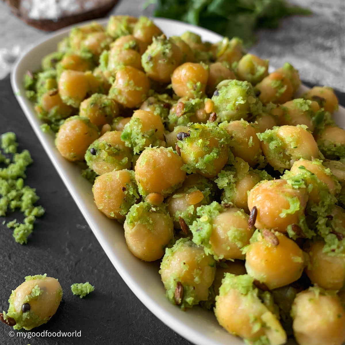 Chickpea sundal in a black bowl garnished with fresh coconut and curry leaves.