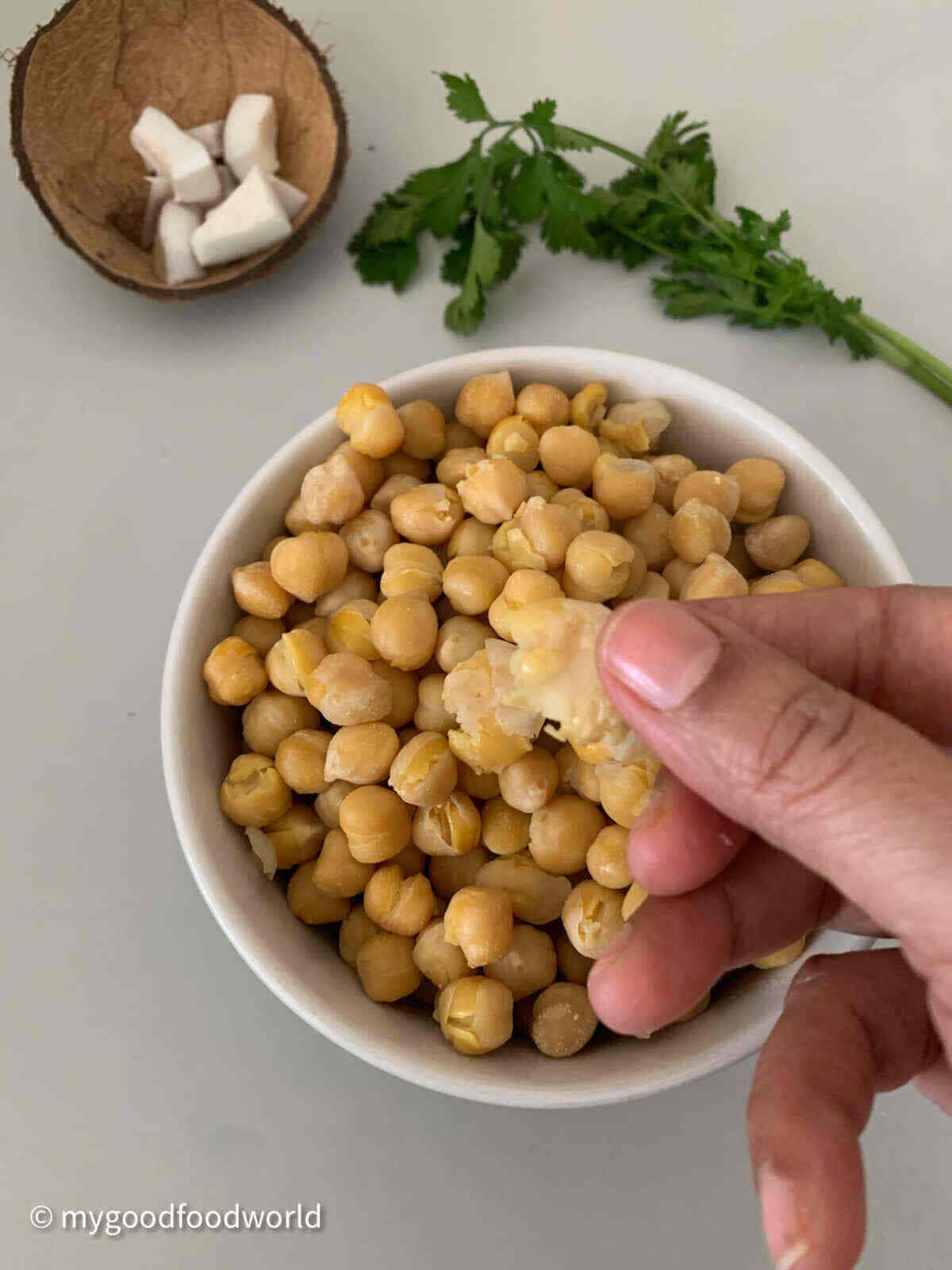 Chickpeas that have been to the perfect texture are being held between two fingers. 