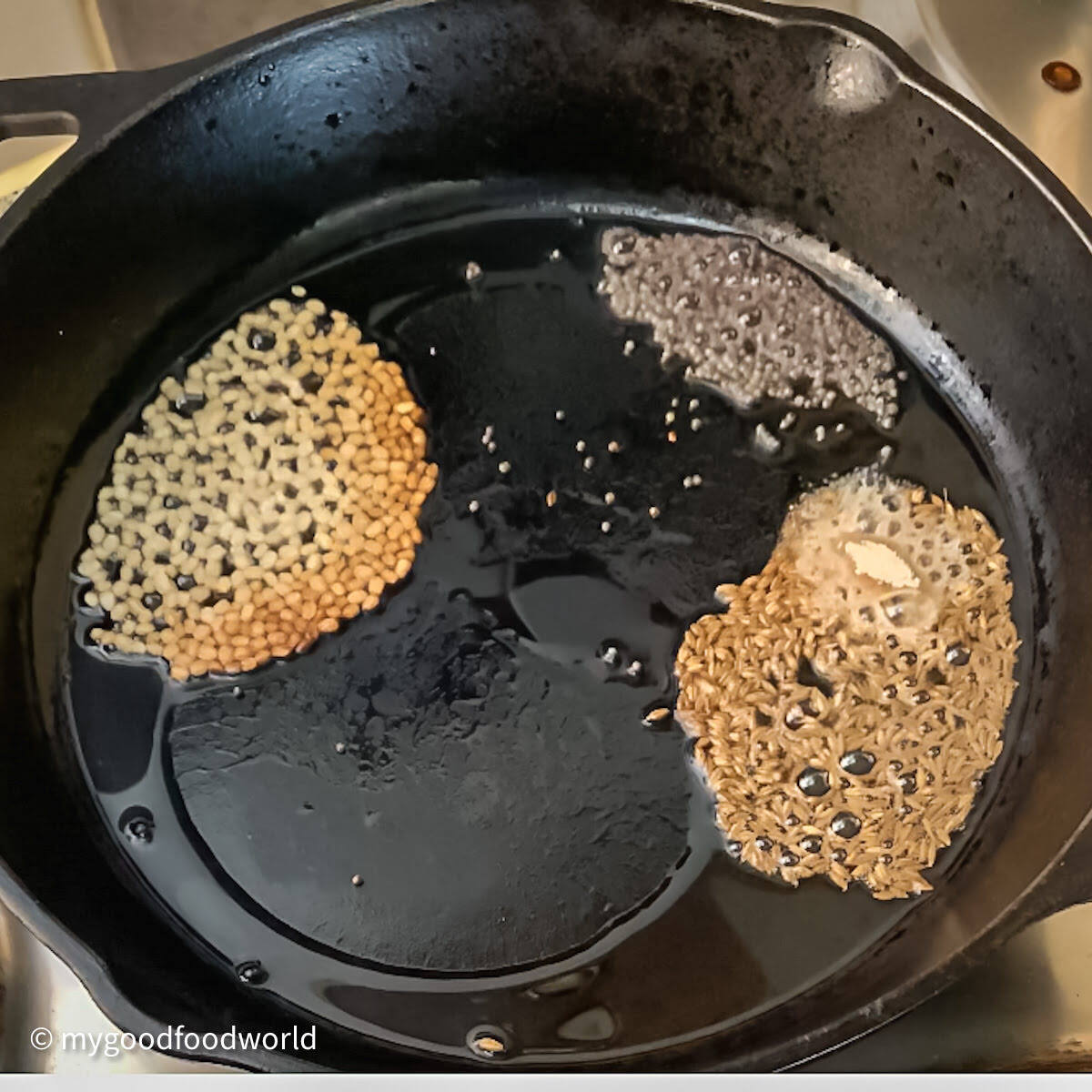 Mustard seeds and curry leaves tempering in a cast iron pan.