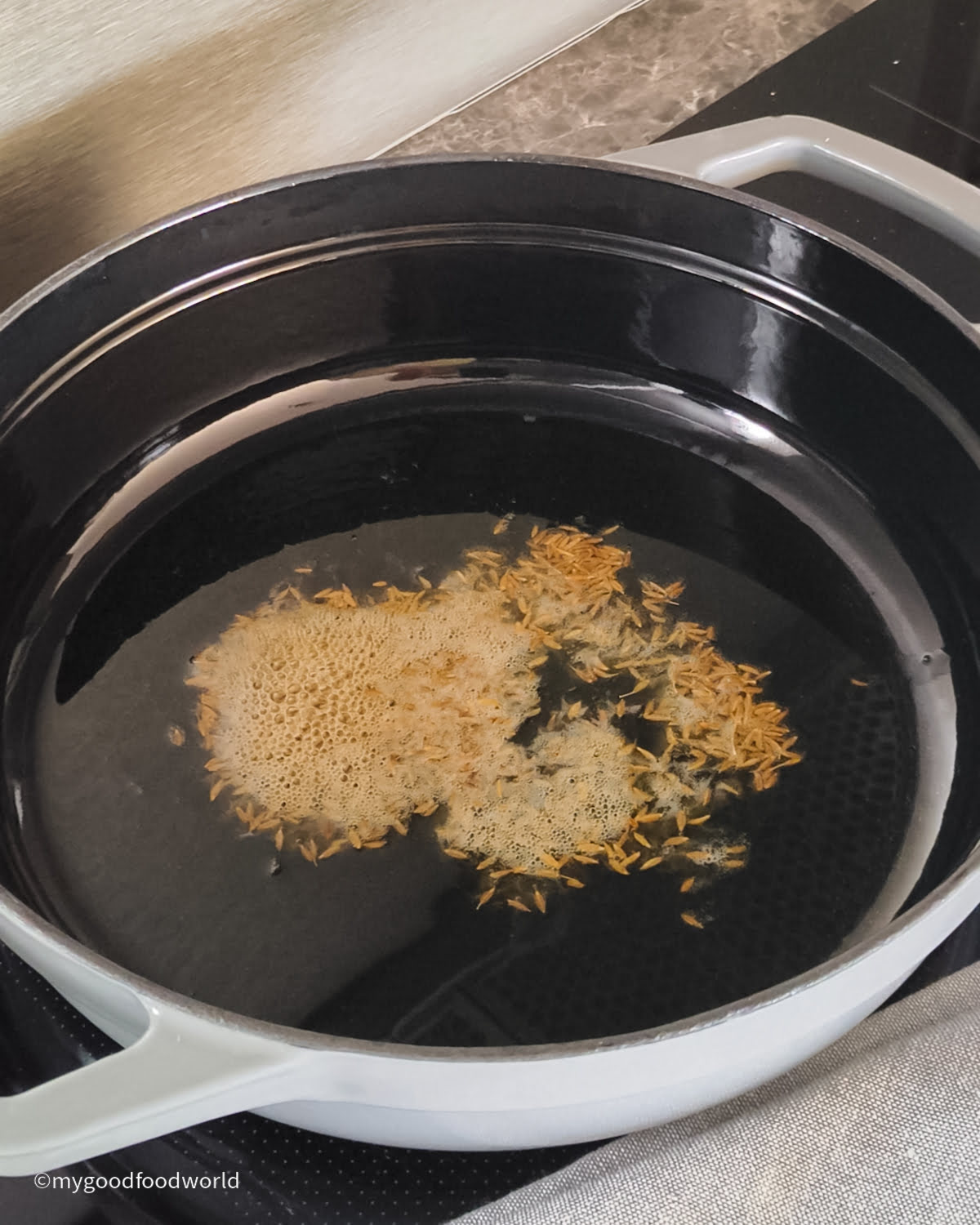 In a wide pan, some whole cumin seeds are sizzling in oil or ghee.