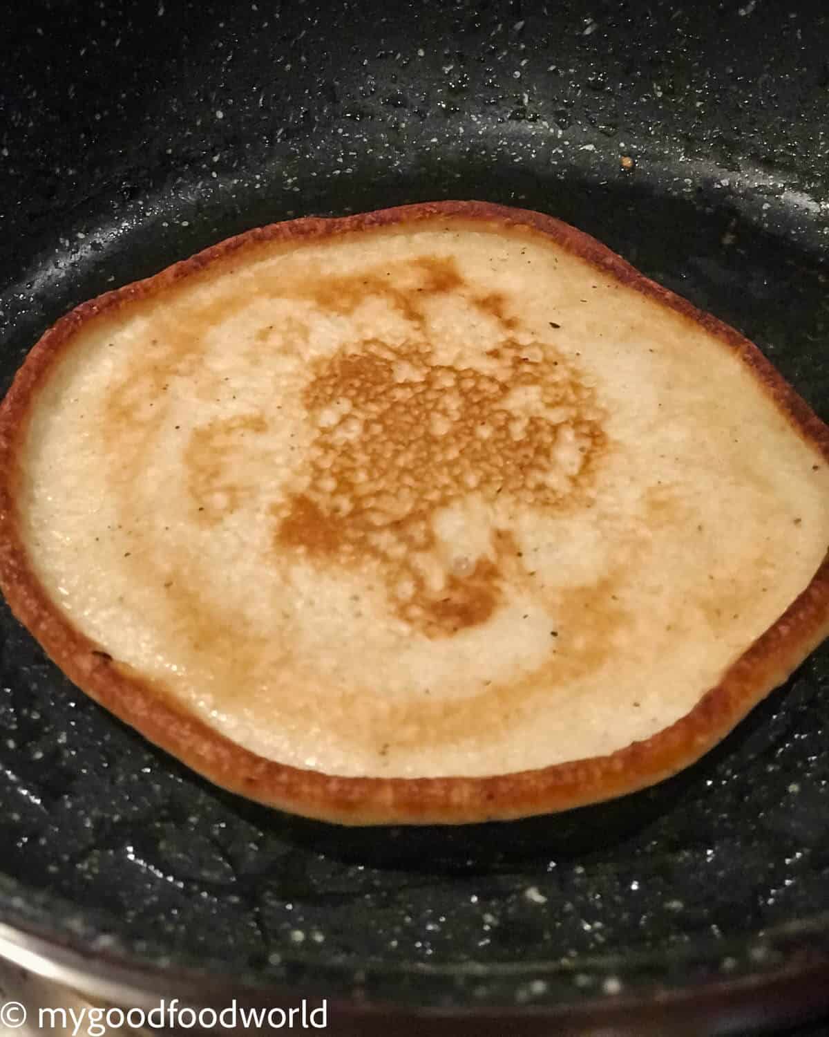 Fluffy pancakes without eggs cooking in a skillet, with golden brown edges after the flip.