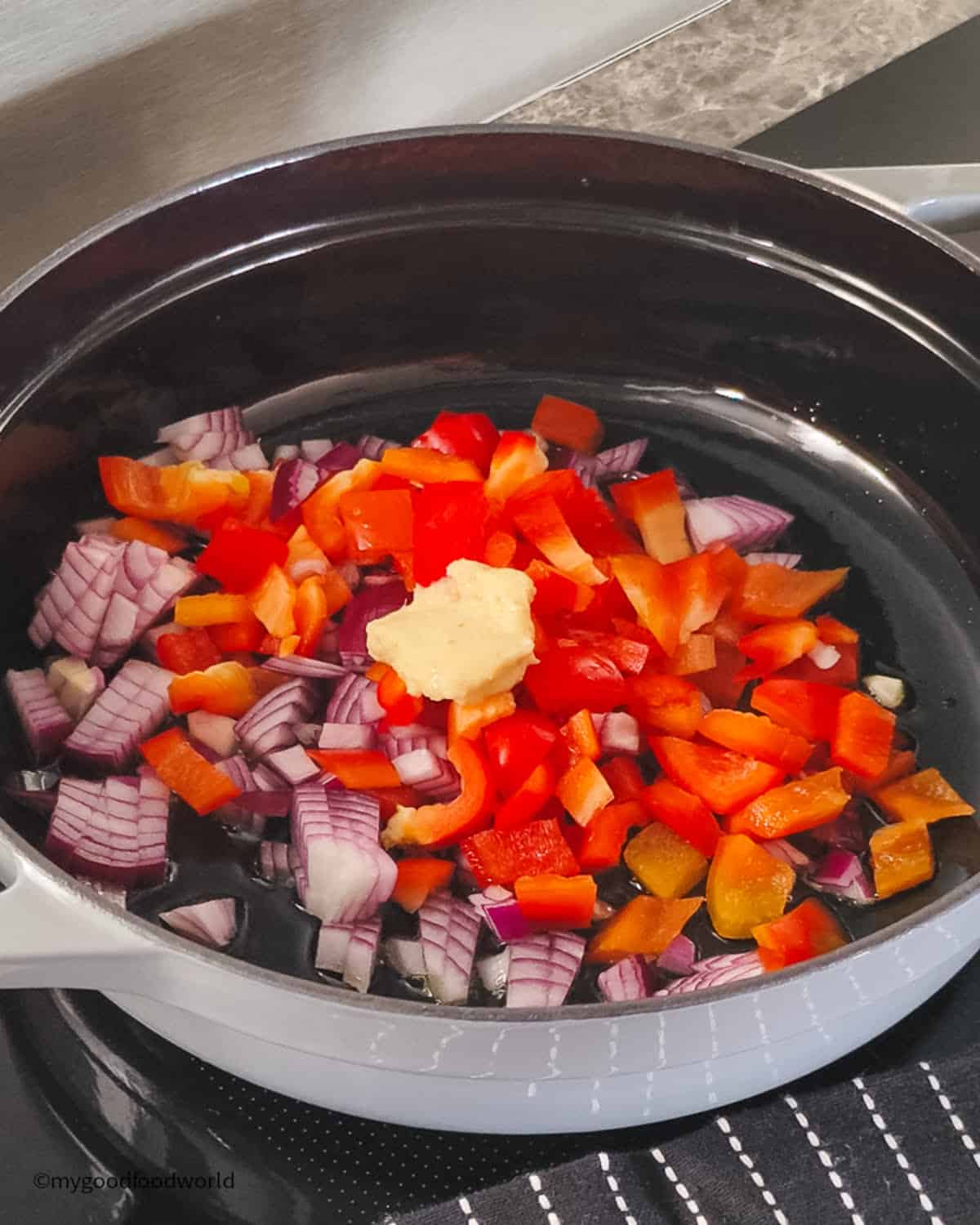 Chopped red onion and red bell pepper with a dollop of ginger garlic paste in a black pan.