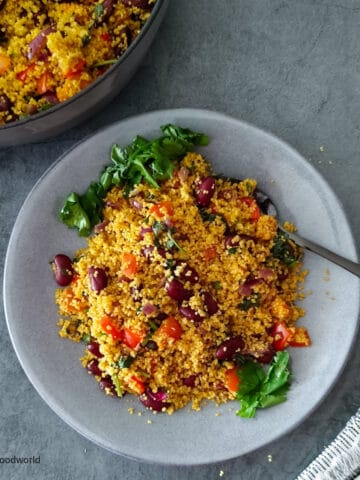 Spicy couscous recipe salad with kidney beans, peppers, and cilantro served on a light grey plate with a fork.