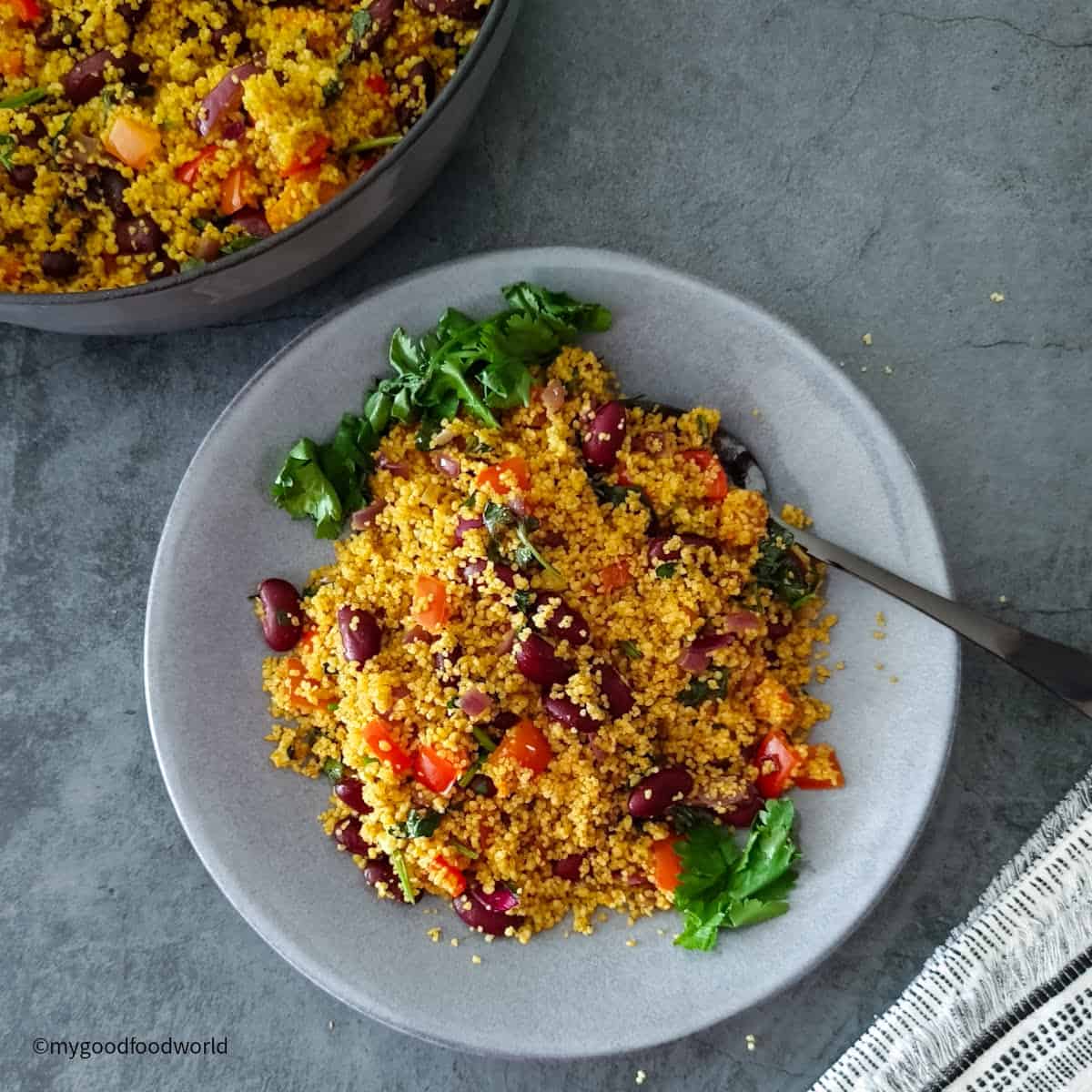 Spicy couscous recipe salad with kidney beans, peppers, and cilantro served on a light grey plate with a fork.
