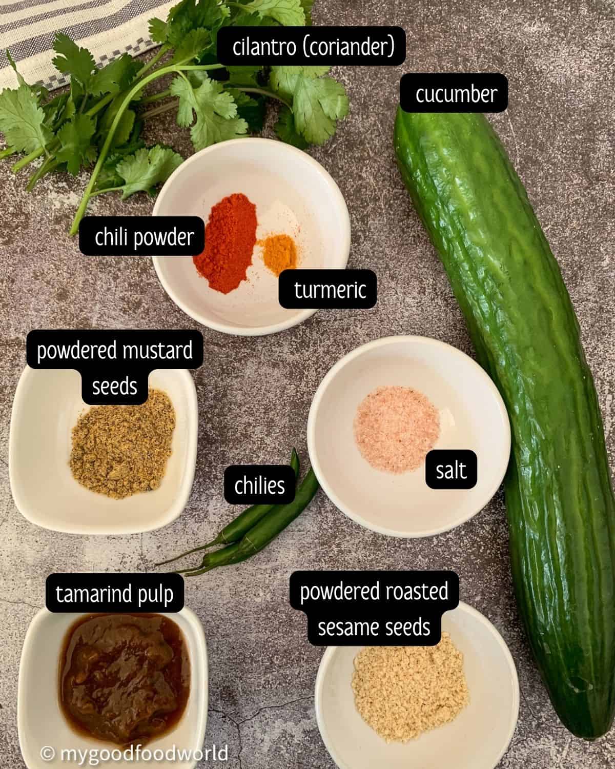 Ingredients for dosakaya mukkala pachadi are placed in small bowls and arranged on a grey textured background.