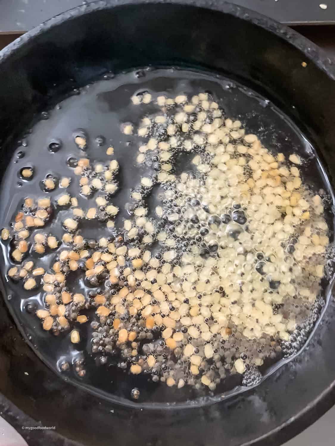 Tempering for dosakaya pachadi - urad dal and mustard seeds frying in oil in a cast iron pan.