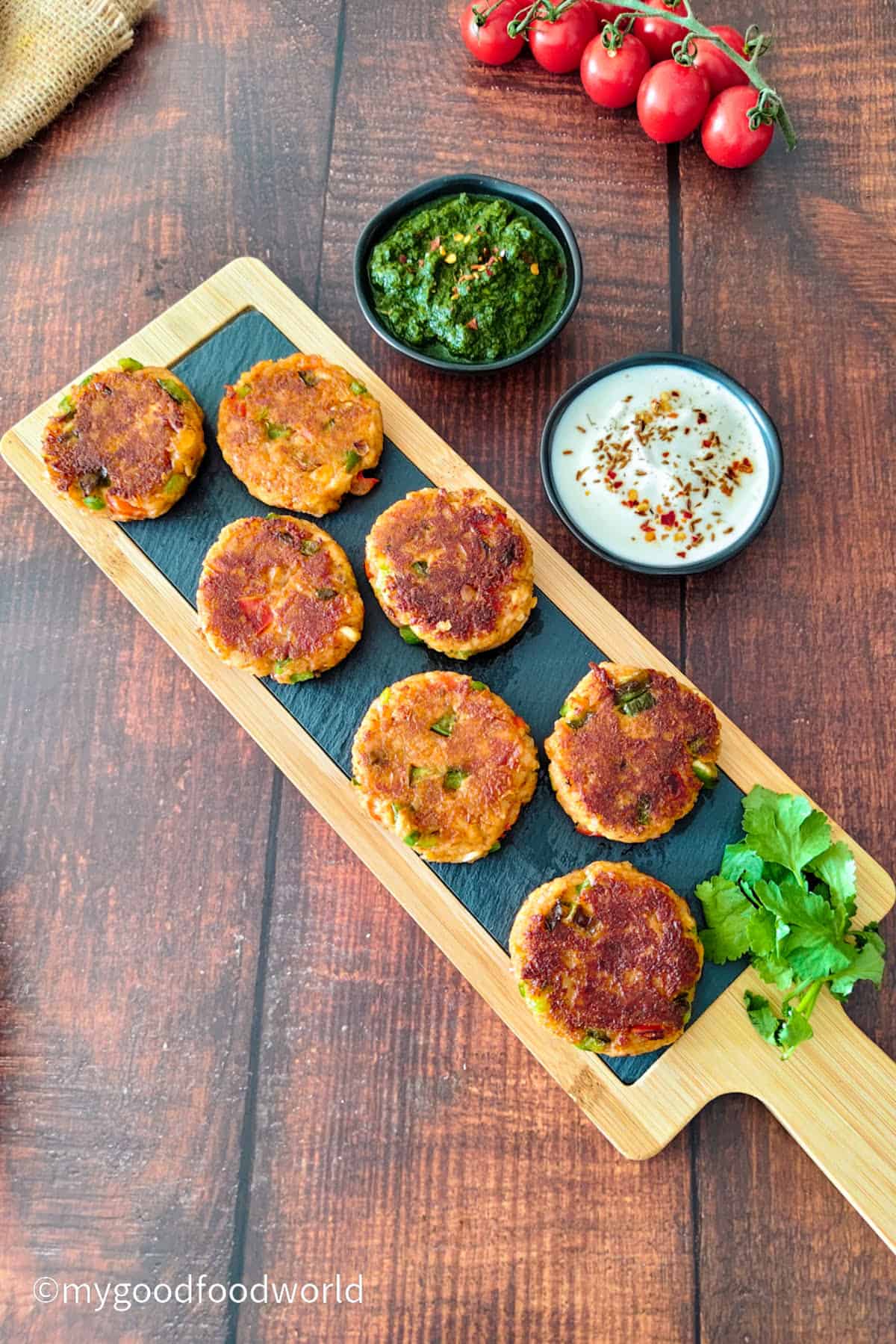 Walnut paneer cutlets with bell pepper on a wooden board with green chutney and yogurt dip.