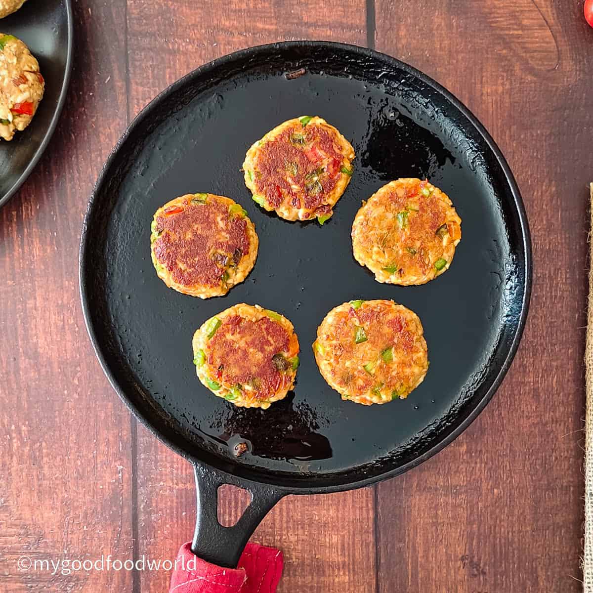 Five golden paneer tikkis, pan-fried in a cast-iron skillet.