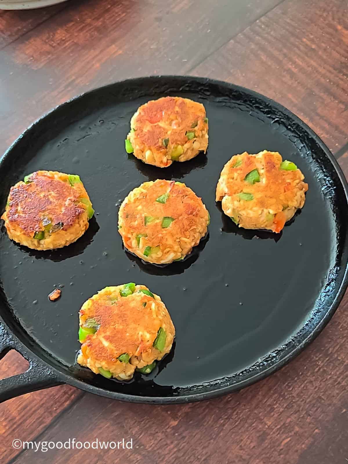 Golden fried paneer tikki patties cooking in a cast-iron pan, crisped on top.
