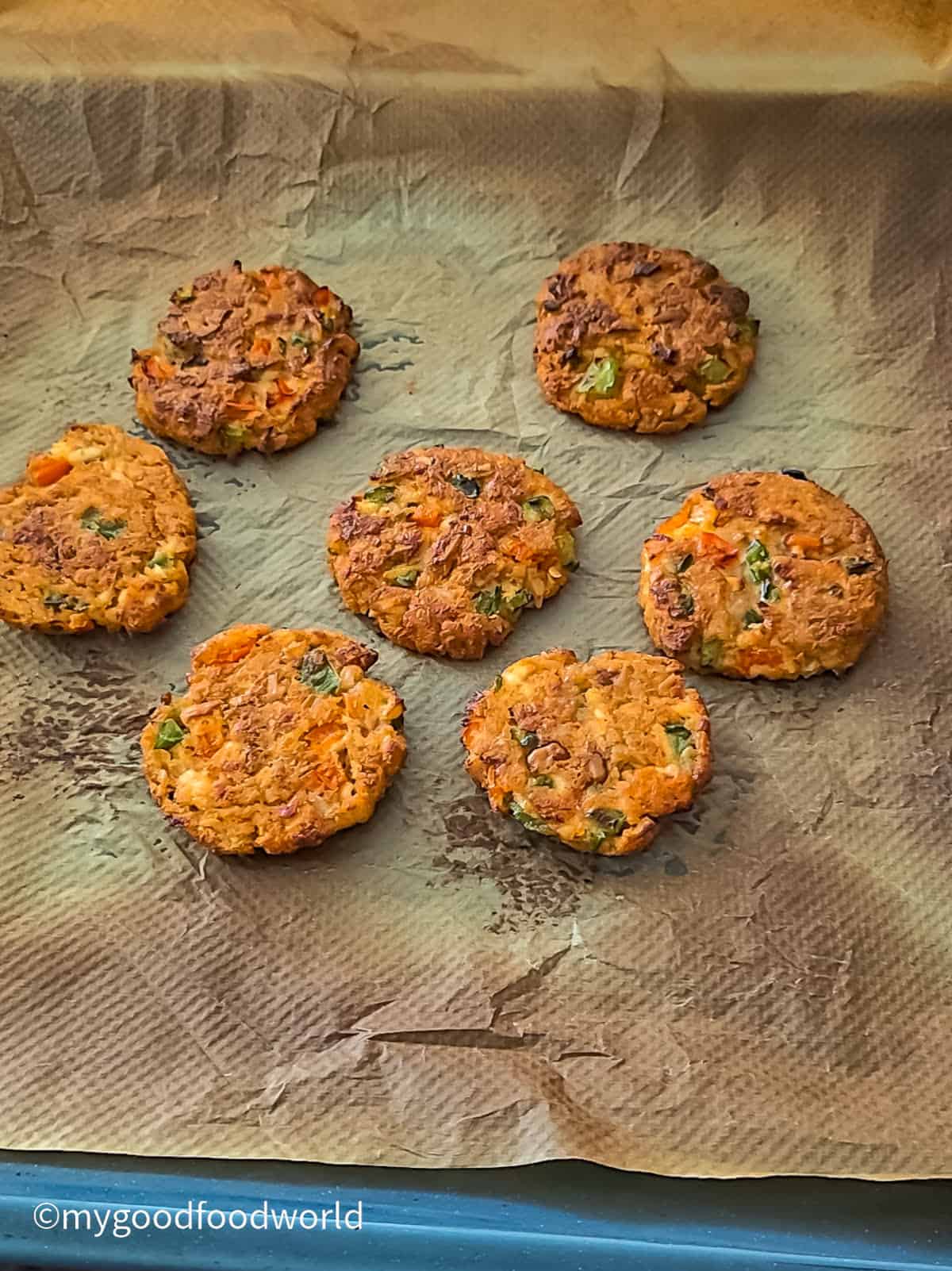 Oven-broiled paneer tikkis on a parchment-lined tray with a browned, crisp crust.