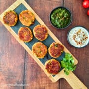 Smoky walnut paneer cutlets served on a wooden board with green chutney and yogurt dip.