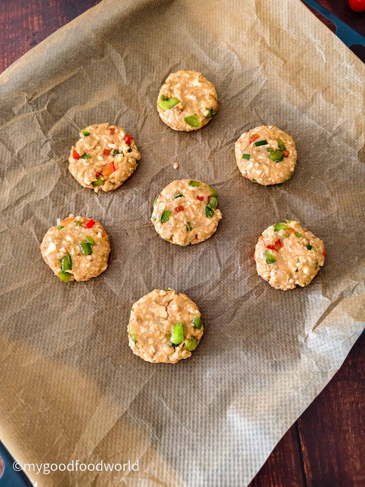 Uncooked paneer cutlets arranged on a parchment-lined tray, ready to be grilled.