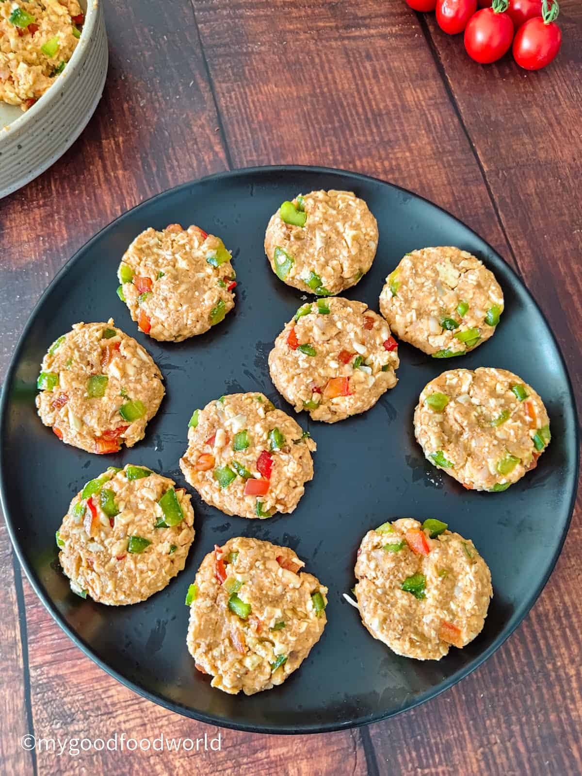 Nine uncooked paneer and potato cutlets shaped into small rounds on a plate.